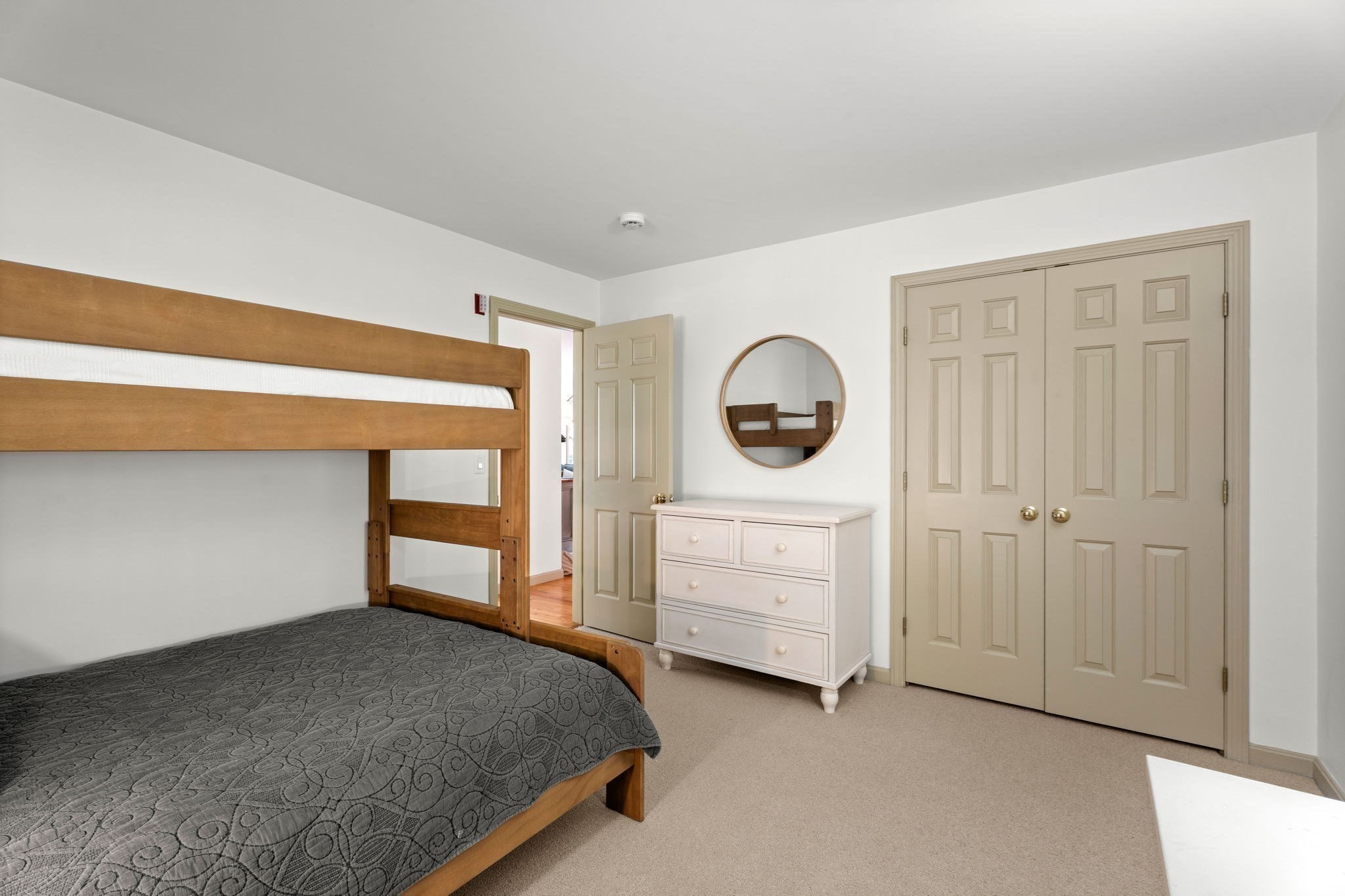 Bedroom with a wooden bunk bed, white dresser, round mirror, and beige double closet doors.