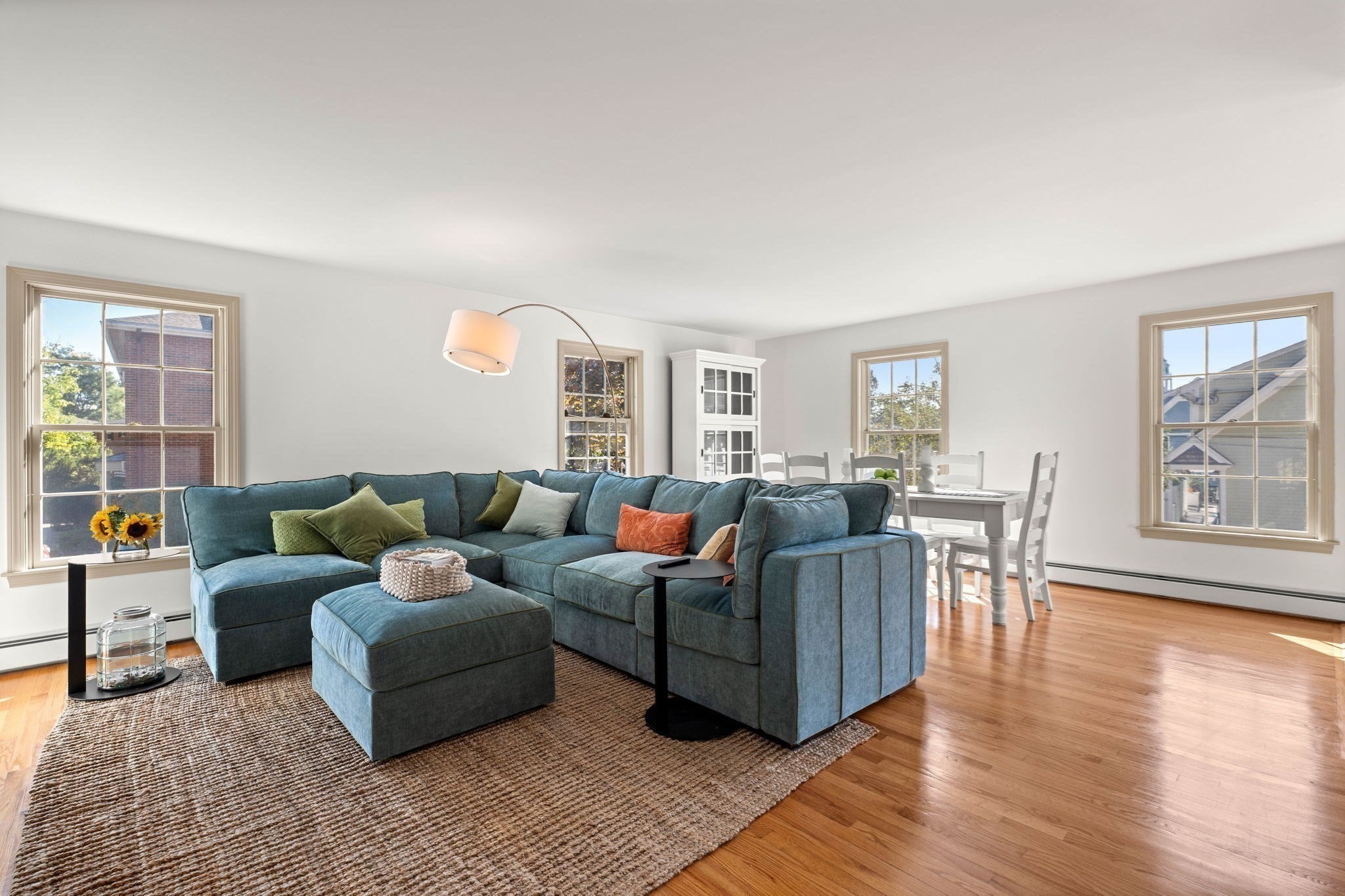 Living room with a blue sectional, woven rug, hardwood floors, and a dining area by the windows.