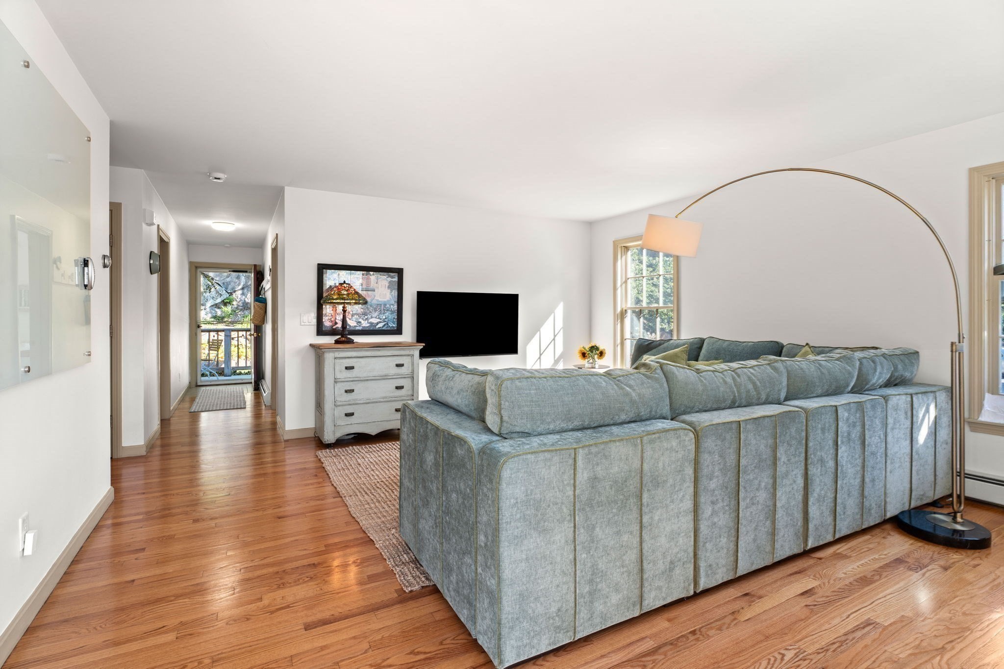 Bright living room with a blue-gray sectional, hardwood floors, and a tall arched floor lamp.