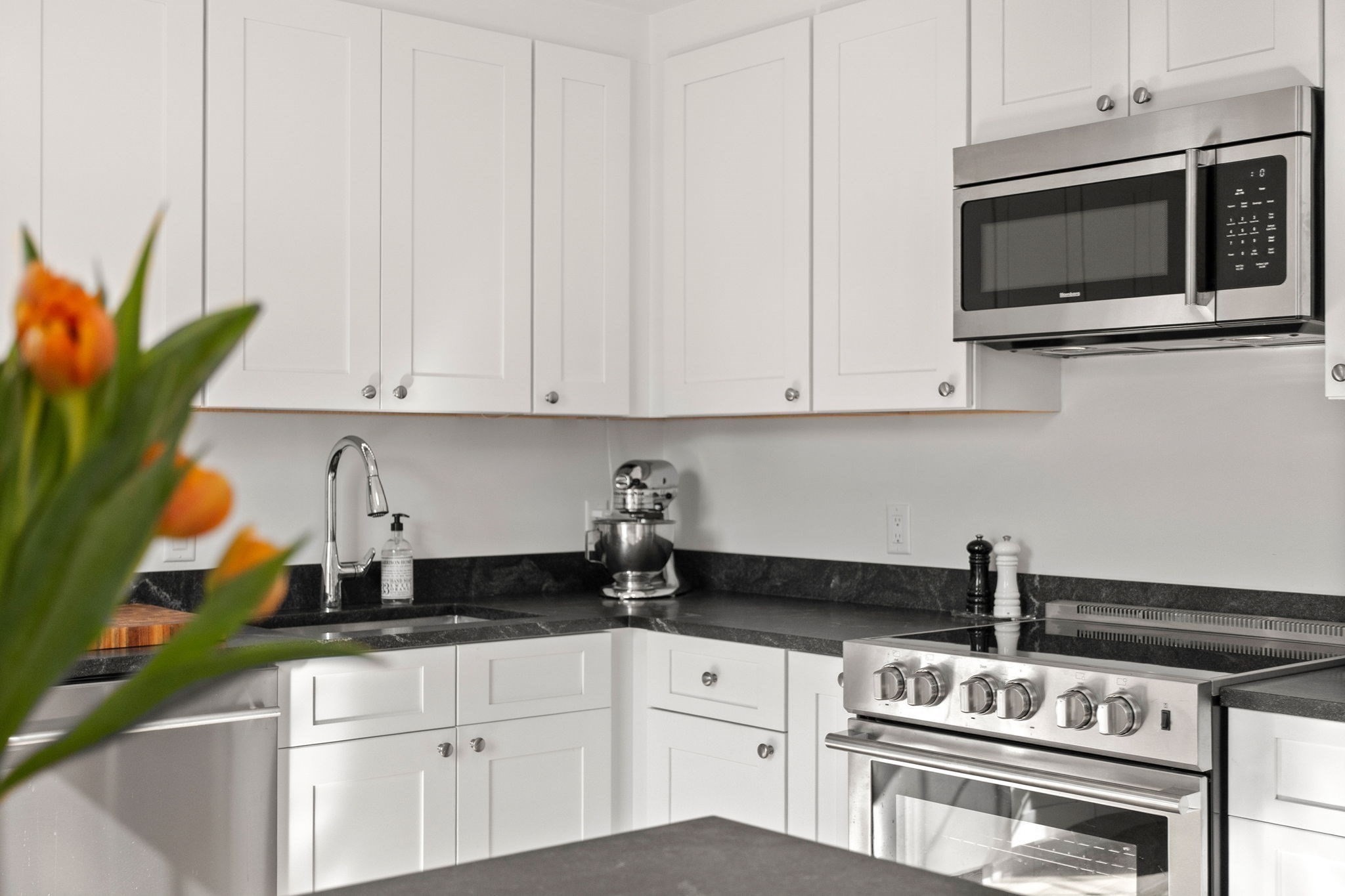 Modern kitchen with white cabinets, dark countertops, stainless steel appliances, and orange tulips in the foreground.