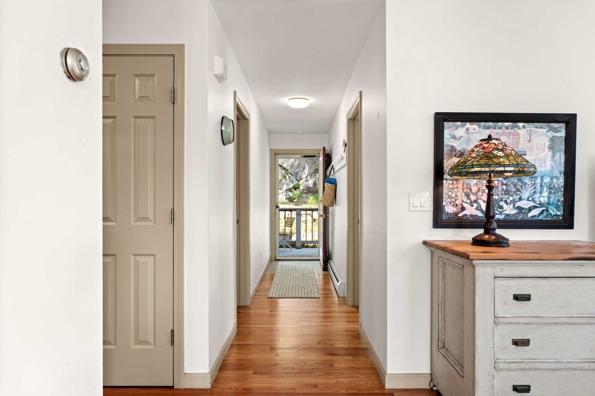 Hallway with hardwood floors, beige doors, and a glass door opening onto a small deck.