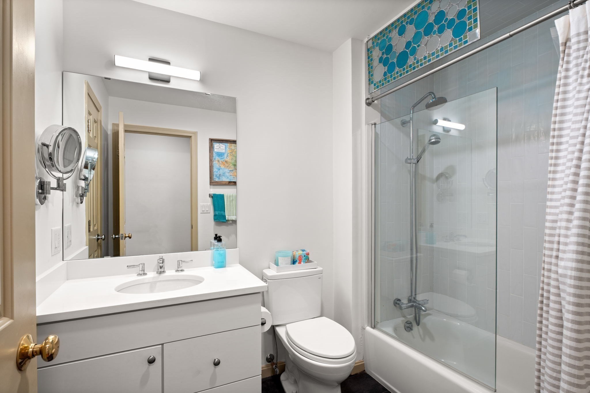 Bathroom with a white vanity, glass shower panel, bathtub, and blue mosaic tile accent.