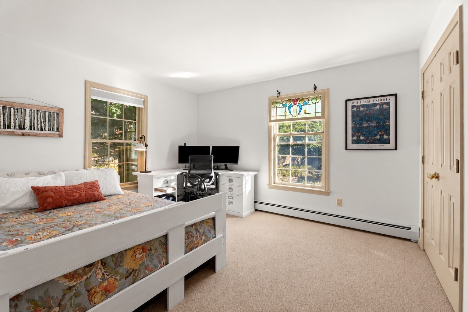 Bright bedroom with a white daybed, dual-monitor desk, and stained-glass window panel.