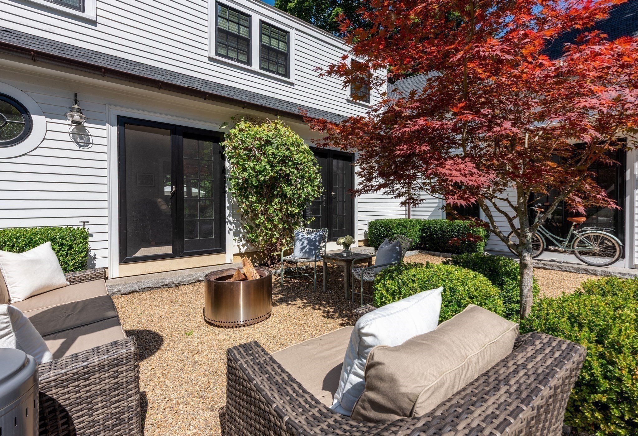 Furnished gravel patio with wicker seating, a fire pit, and a red-leaved Japanese maple.