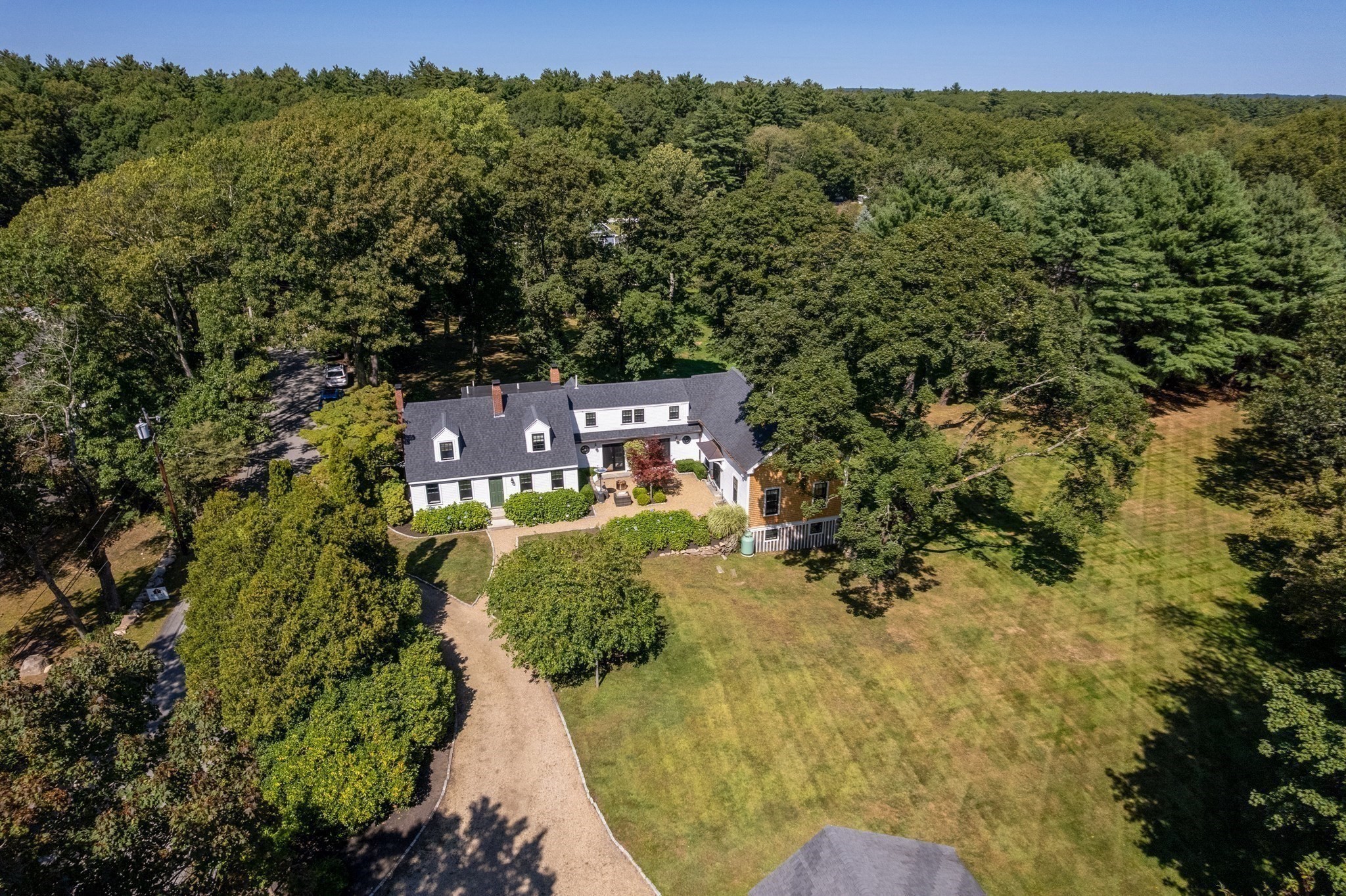Aerial view of a white house amid mature trees, a broad lawn, and a curved gravel driveway.