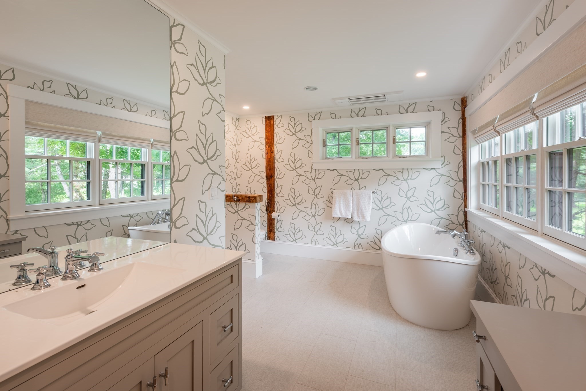 Bathroom with a freestanding soaking tub, double vanity, leafy wallpaper, and abundant windows.