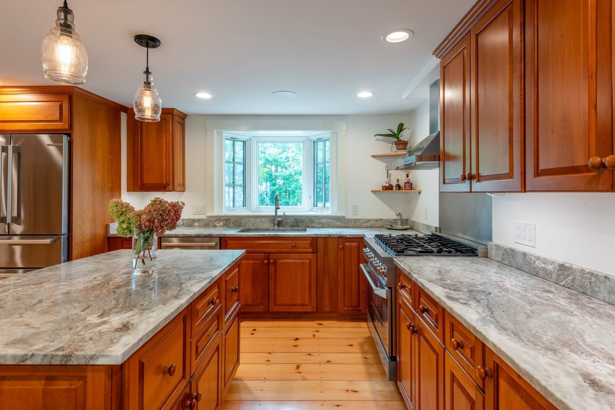 Kitchen with warm wood cabinets, stone counters, and a bay window above the sink.
