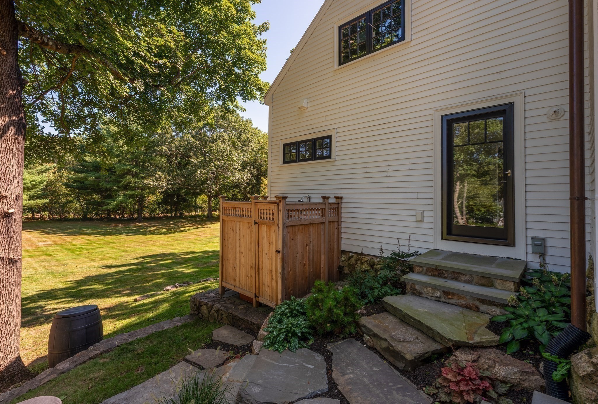 House exterior with stone steps, a wooden privacy enclosure, and a tree-shaded lawn.