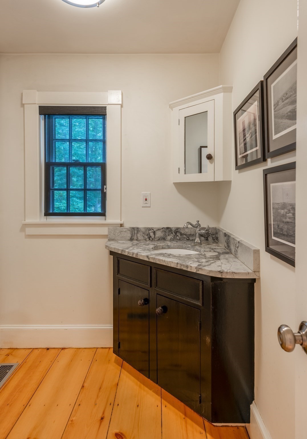 Bathroom vanity with a veined marble counter, dark cabinetry, mirrored cabinet, and black-framed window.