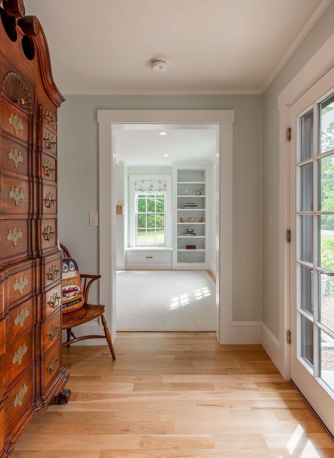 Bright hallway with hardwood floors, an antique chest, and a view of built-in shelves through the doorway.