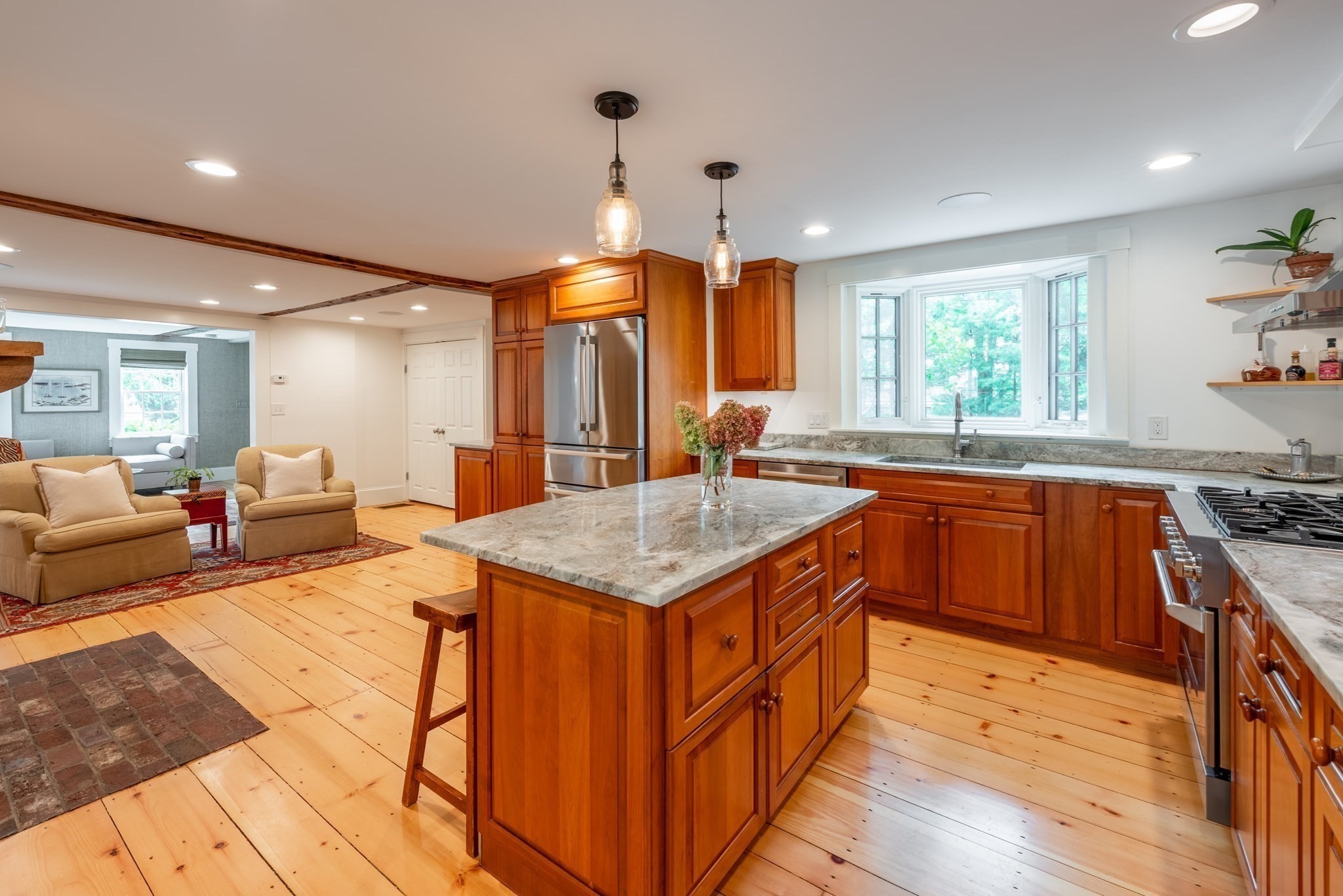 Kitchen with a large stone-topped island, warm wood cabinetry, and an adjoining sitting area.