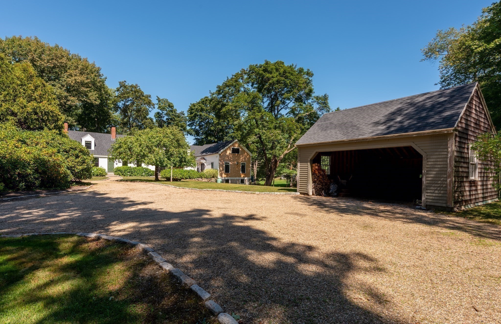 Home and detached shingle-sided garage beside a broad gravel driveway and mature trees.