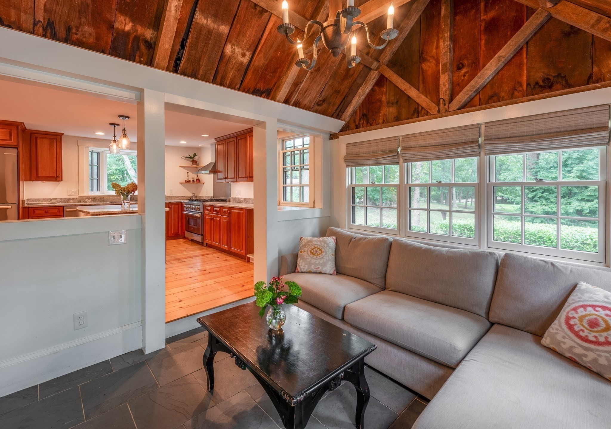 Living room with a gray sectional, exposed wood-beam ceiling, and windows overlooking trees.