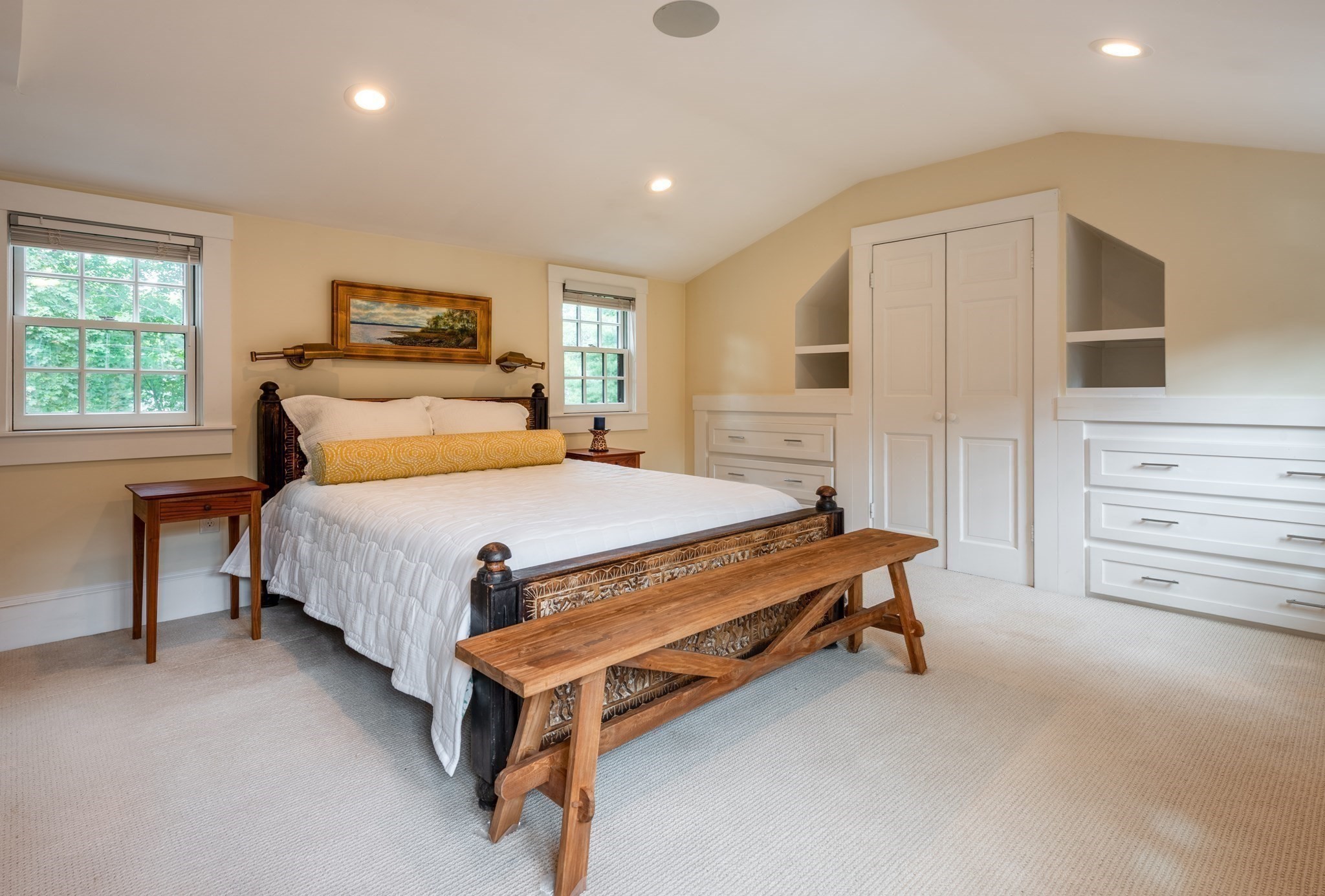 Bedroom with a carved wooden bed, long bench, and built-in white cabinetry.