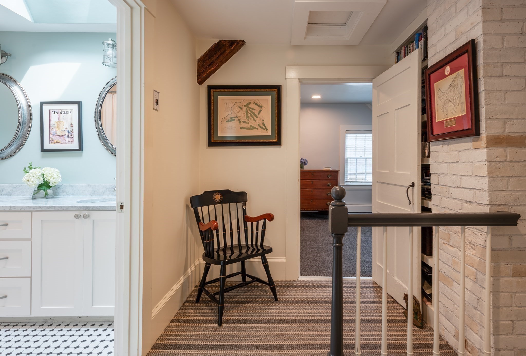 Upstairs landing with a black spindle-back chair, striped carpet, built-in bookshelves, and an adjoining bright bathroom.