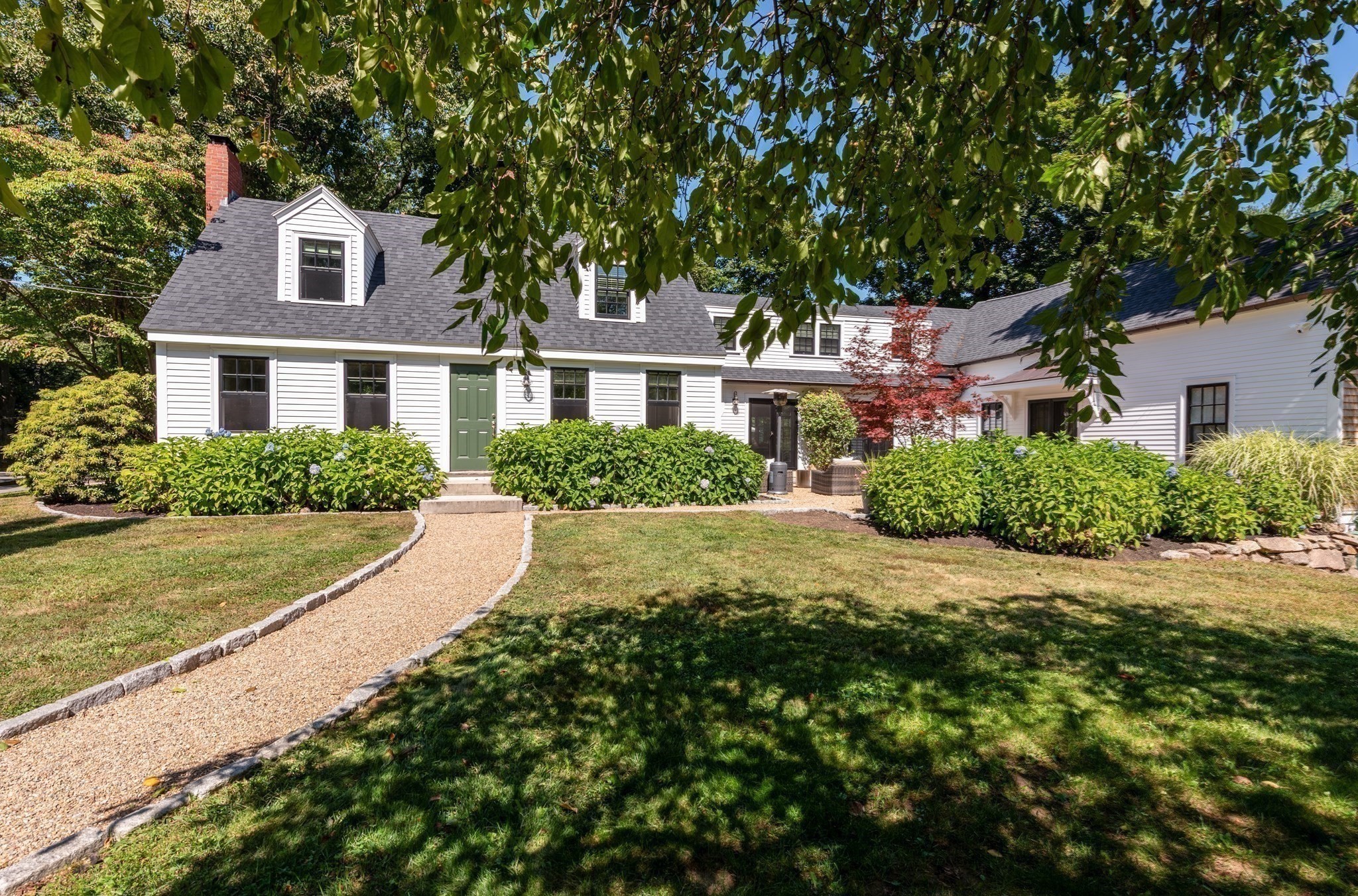 White two-story house with dormer windows and green front door, approached by a curved gravel path.