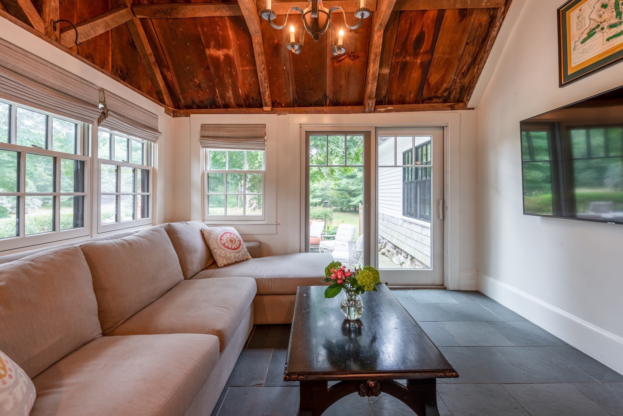Living room with a taupe sectional, exposed wood ceiling, large windows, and glass door to the yard.