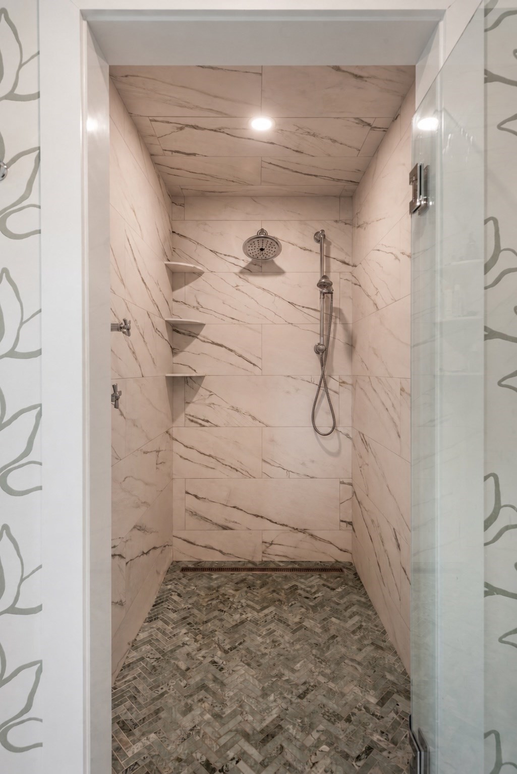 Walk-in shower with marble-look tile, mosaic floor, corner shelves, and rain showerhead.