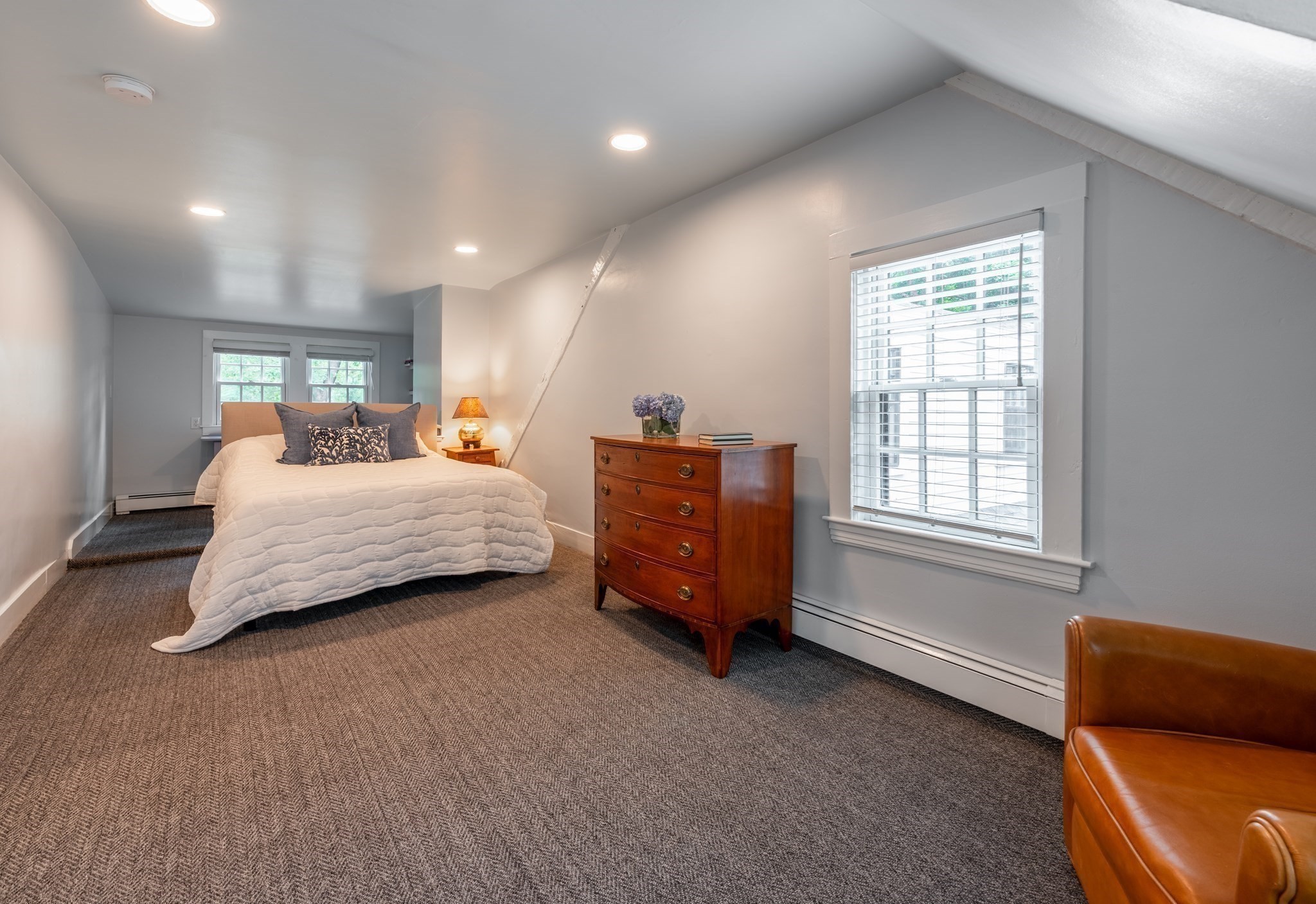 Attic bedroom with a white-quilted bed, wooden dresser, and sloped ceiling.
