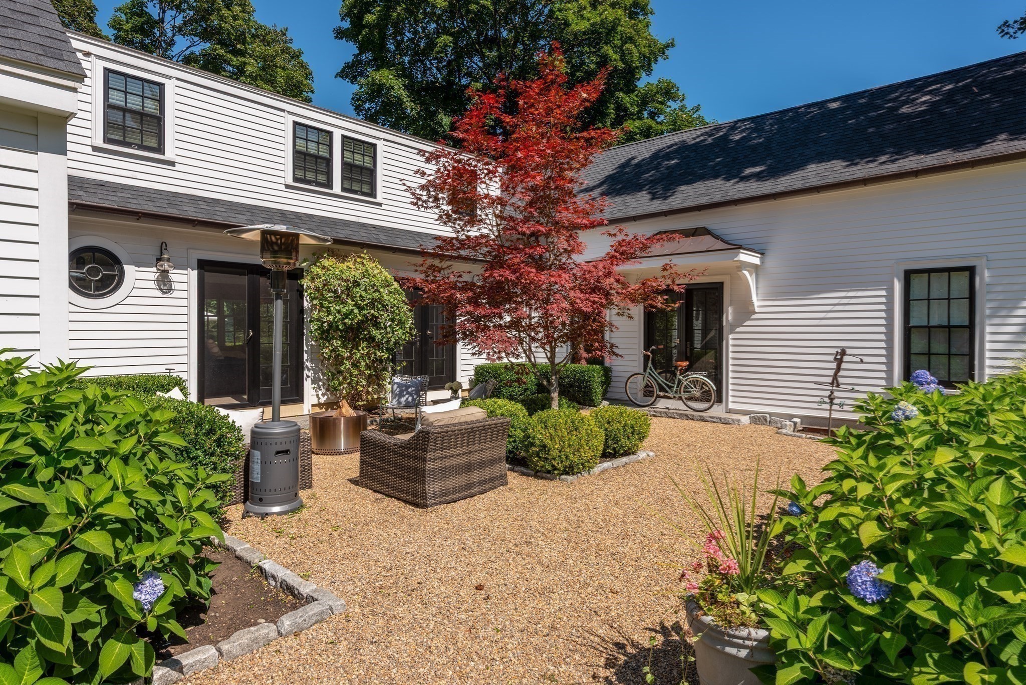 Landscaped gravel courtyard patio with wicker seating, a patio heater, and red-leaf Japanese maple.