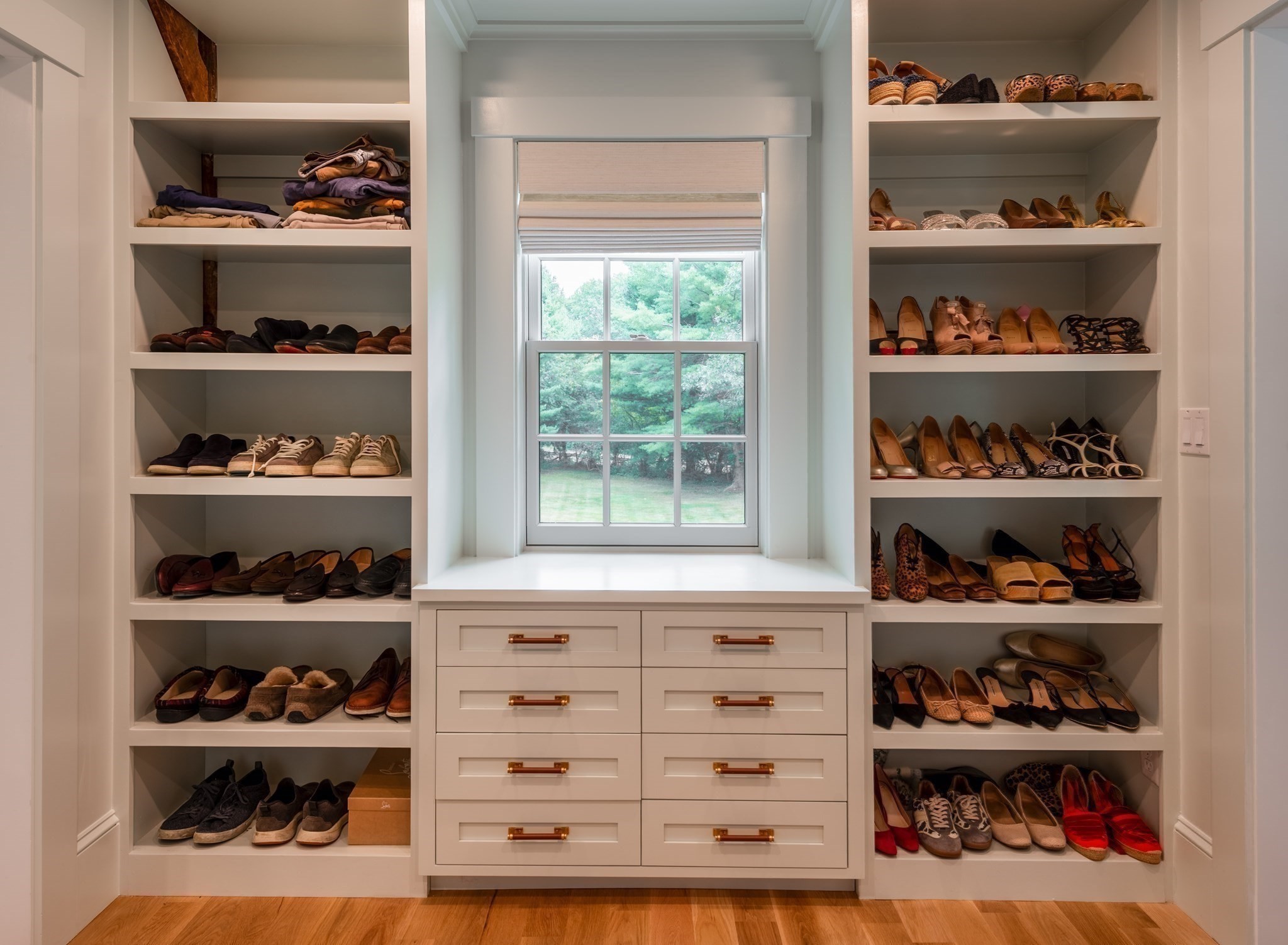 Walk-in closet with shoe shelves flanking a window and white drawers below.