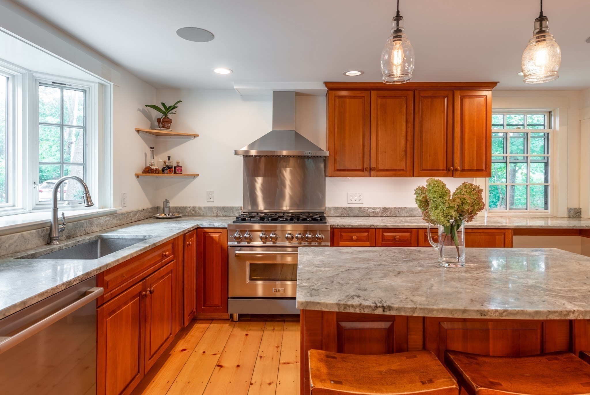 Kitchen with warm wood cabinets, stone counters, a large island, and stainless steel range.