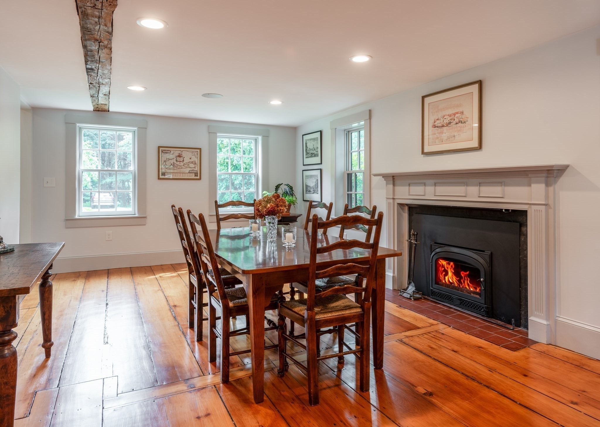 Dining room with a wood table, wide-plank floors, exposed beam, and lit fireplace.