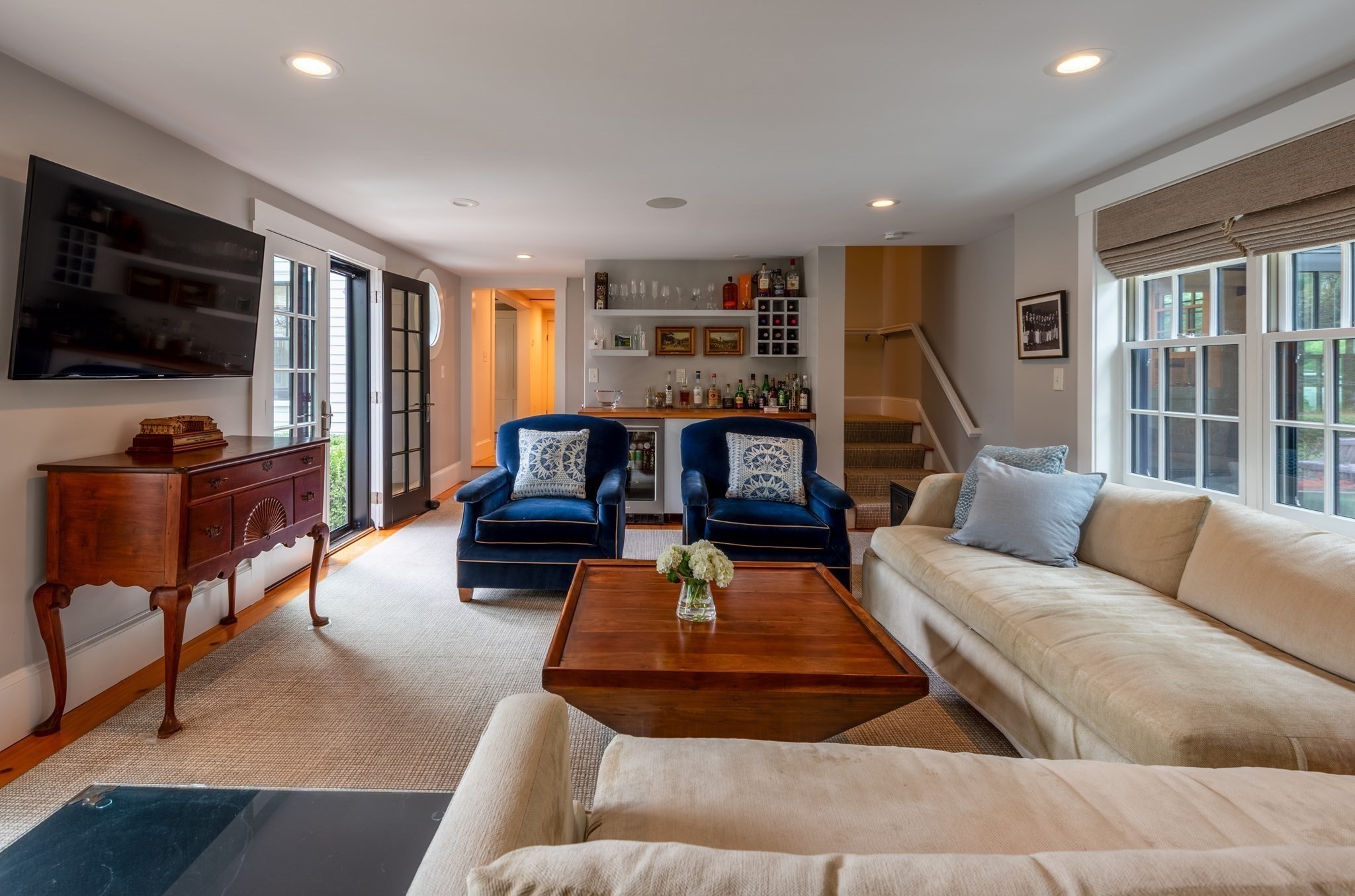 Living room with navy armchairs, a beige sofa, and a built-in bar beside large windows.