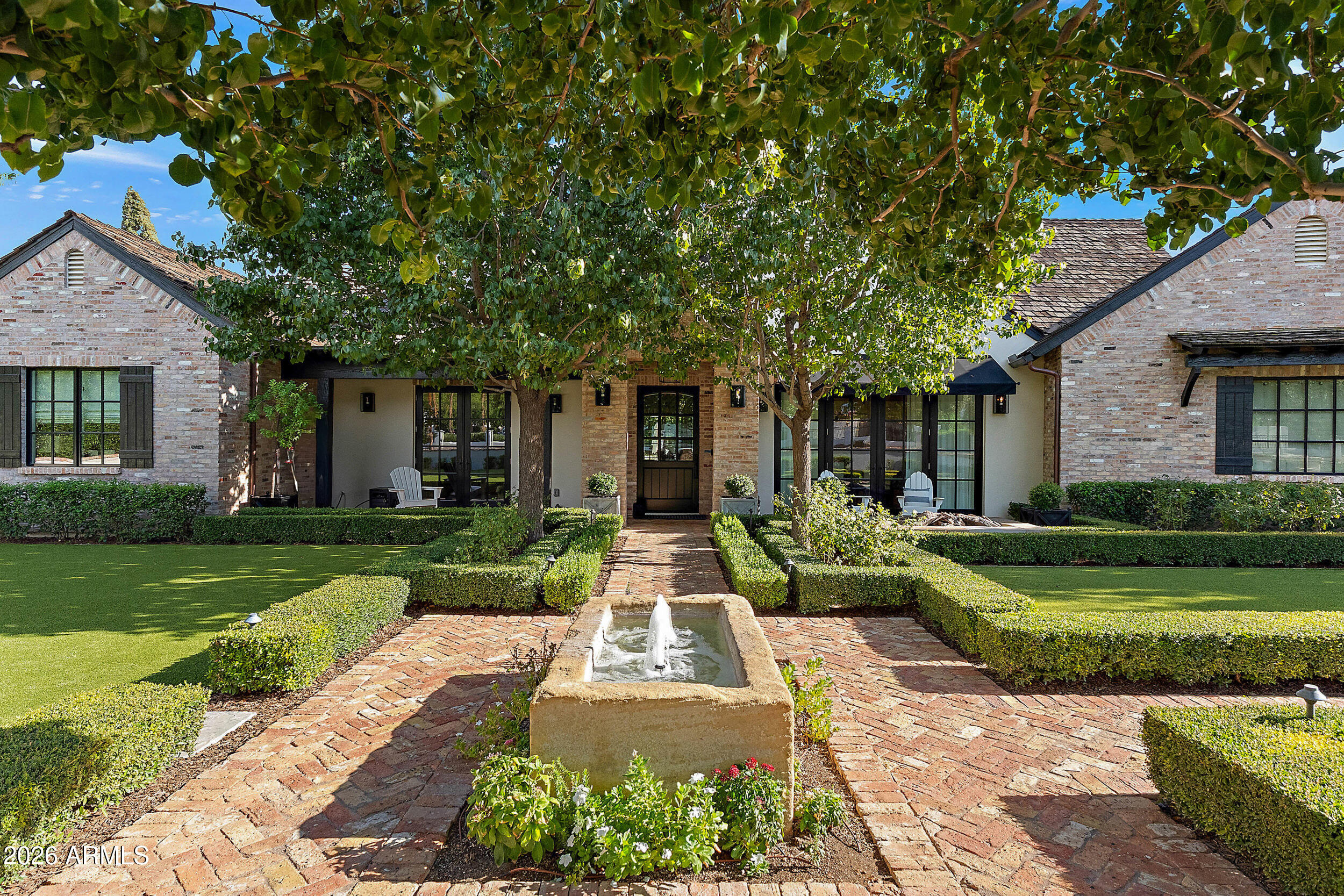 Brick home with a front garden fountain, brick walkway, and mature shade trees.