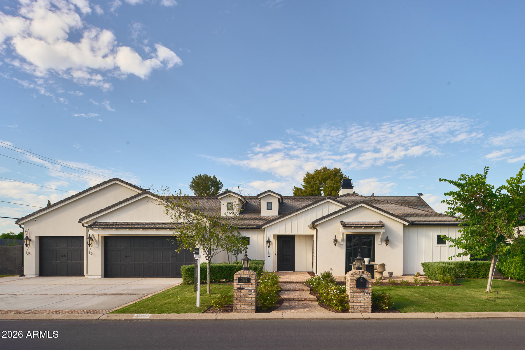 Single-story home with a tile roof, three-car garage, landscaped front yard, and brick entry path.