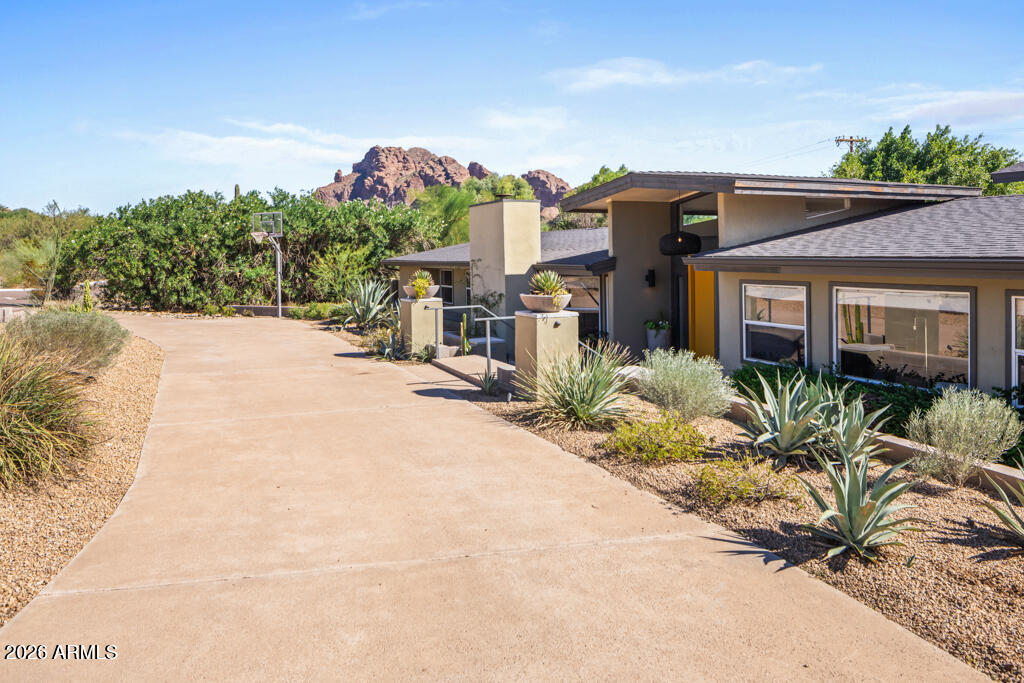 Modern desert home with a broad driveway, desert landscaping, and red mountains behind it.