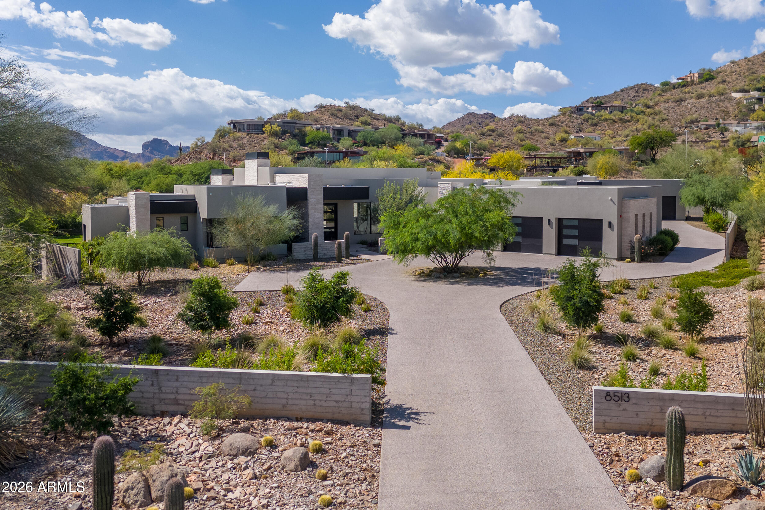 Modern desert home with a curved driveway, mountain foothills, and xeriscaped cactus landscaping.
