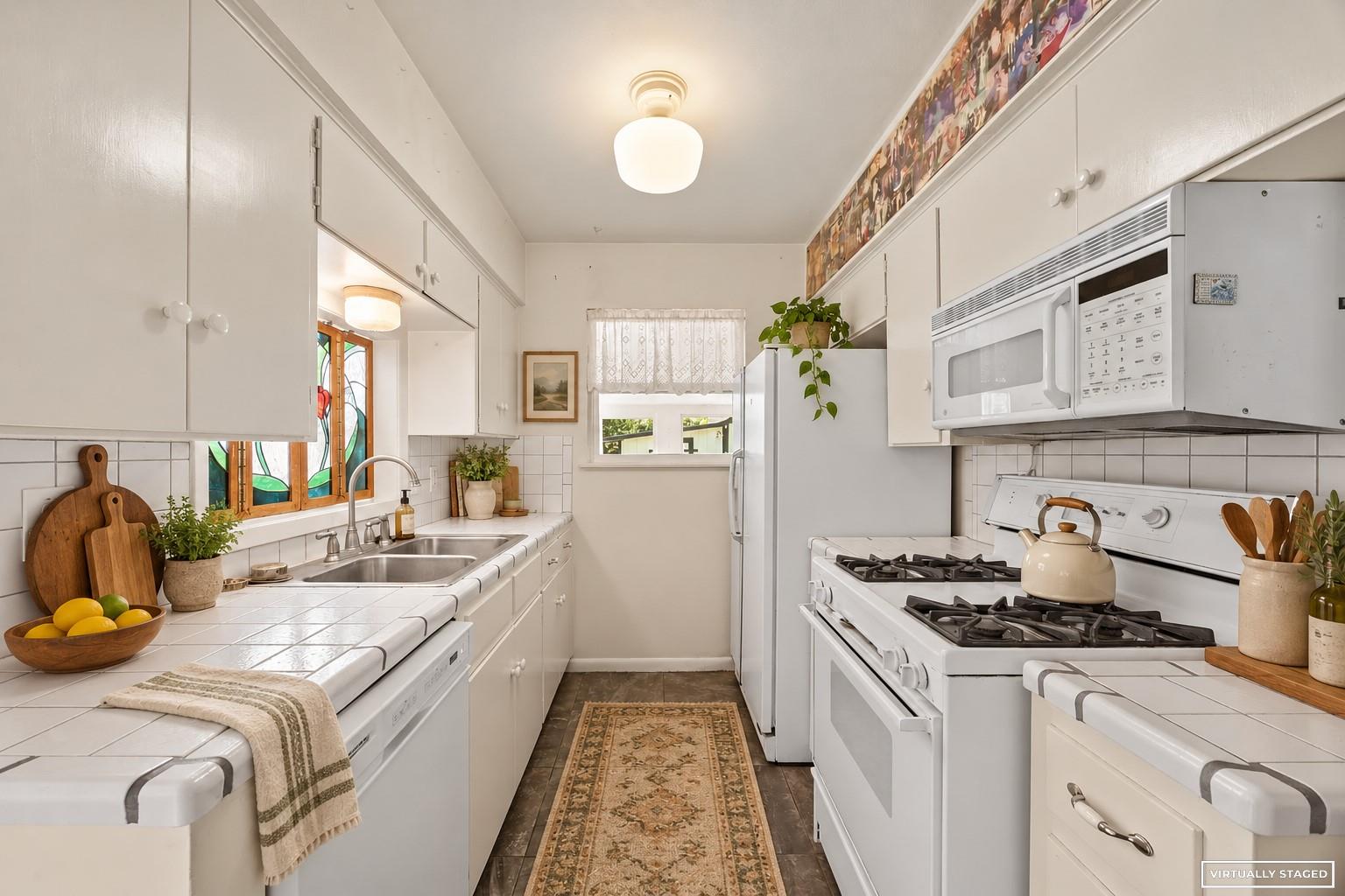 Galley kitchen with white tile counters, gas range, and a colorful stained-glass window.