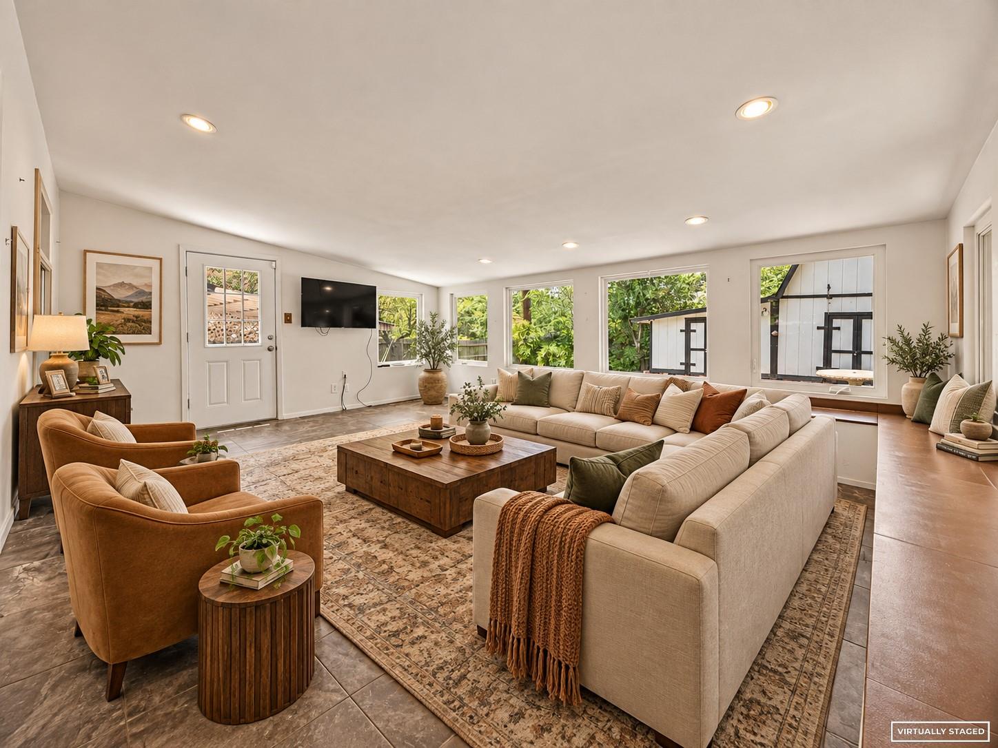 Living room with a cream sectional, caramel armchairs, and wide windows overlooking greenery.