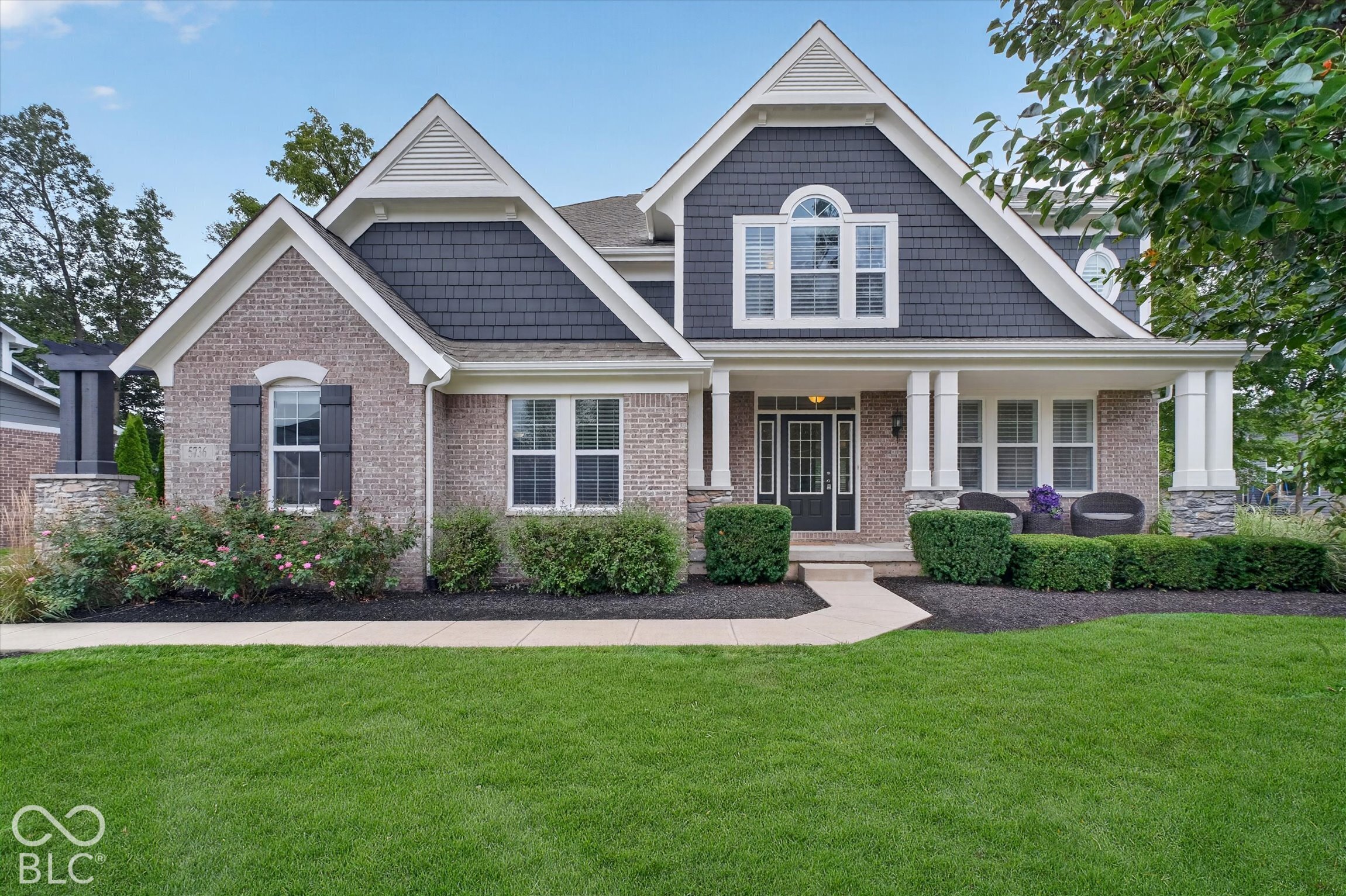 Two-story brick house with dark-shingle gables, a covered porch, and landscaped front lawn.