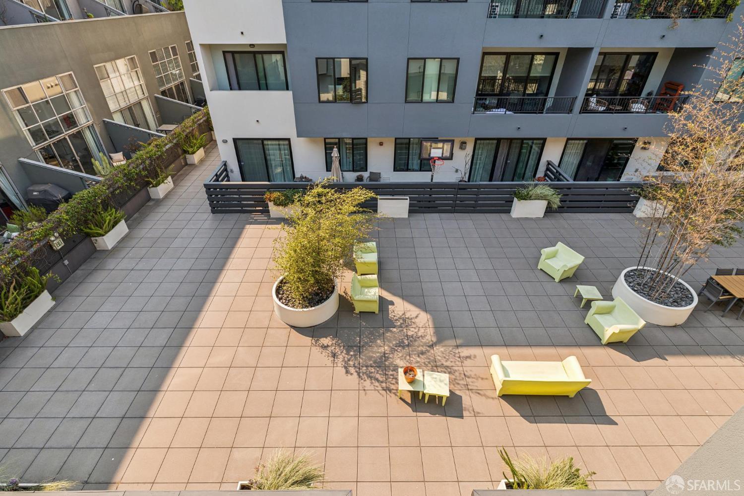 Shared courtyard terrace with pale lounge seating, large planters, and balconies overlooking the tiled patio.