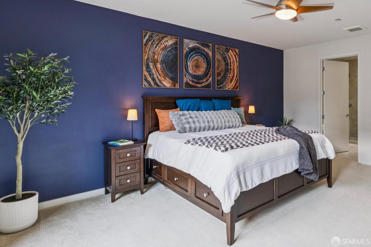 Furnished bedroom with a dark wood bed against a navy accent wall and an open ensuite doorway.
