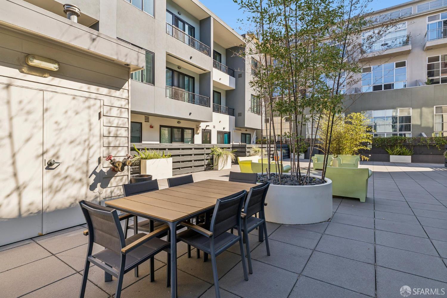Condominium courtyard patio with outdoor dining furniture, lounge seating, and trees in planters.