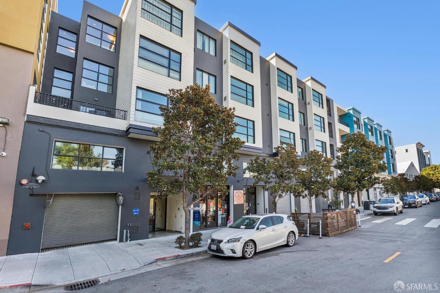 Modern condominium building with charcoal and light siding, large windows, and street-level storefronts.