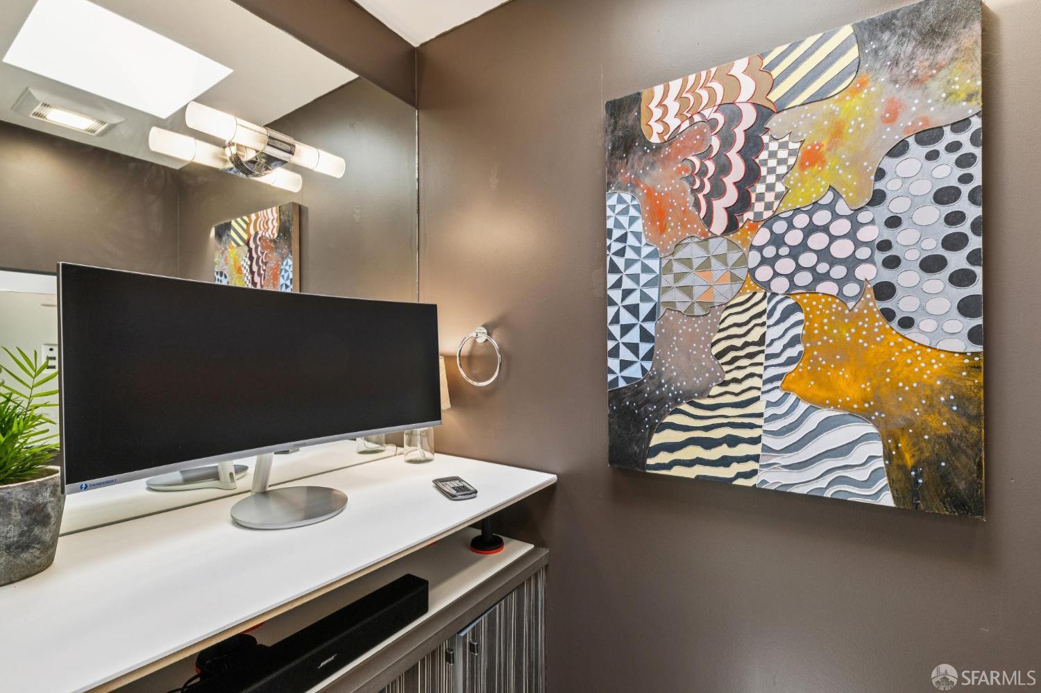 Workstation with a large monitor beneath colorful abstract artwork.