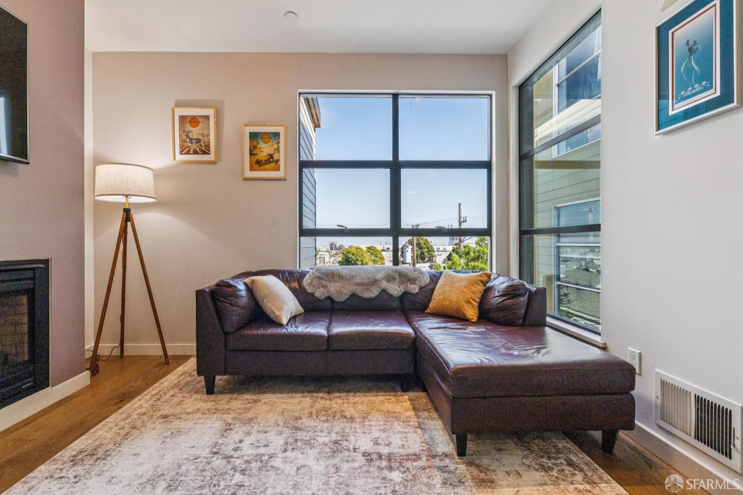 Living room with a leather sectional, fireplace, and large windows overlooking nearby buildings and trees.