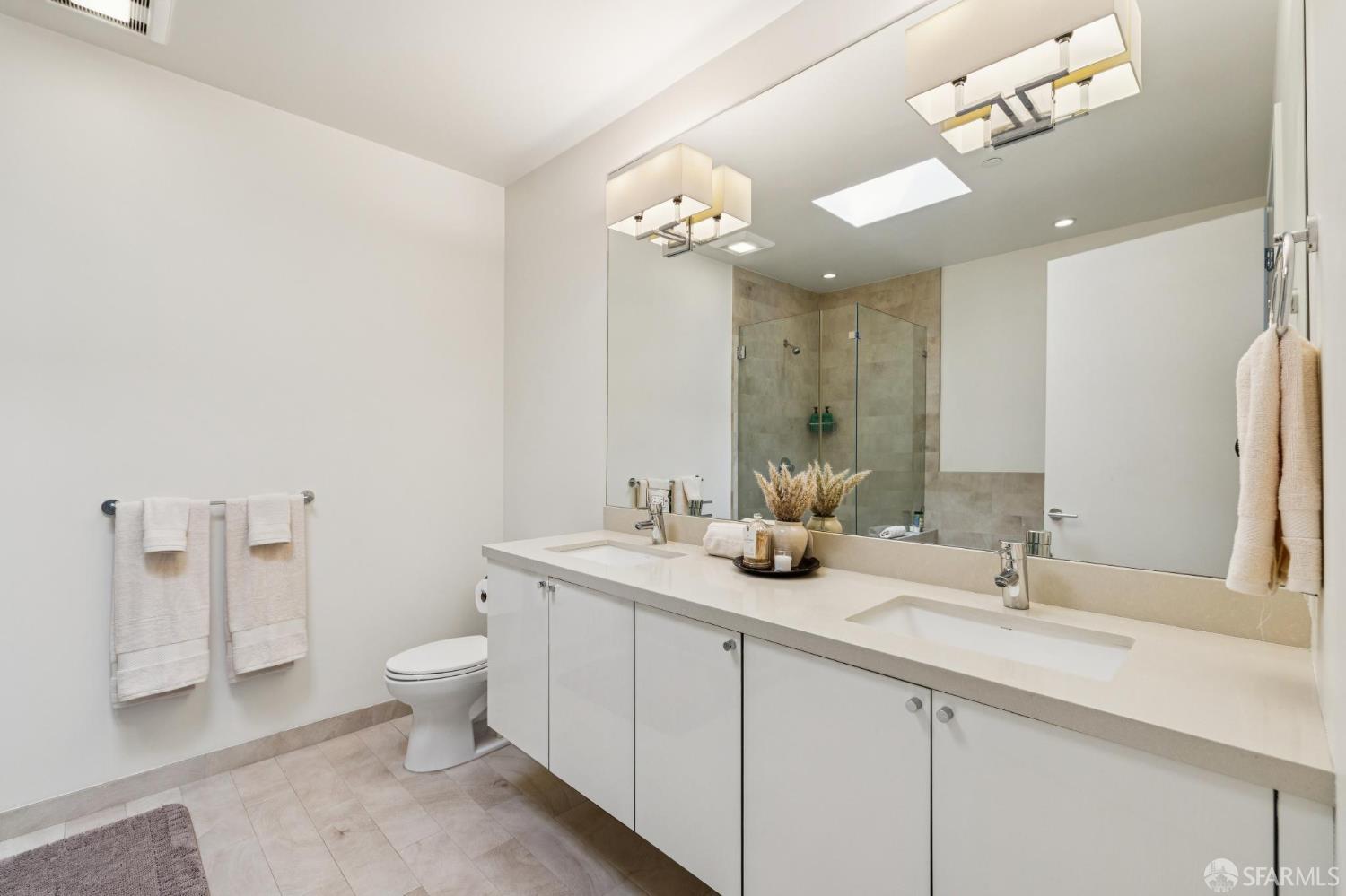 Bathroom with a long double vanity and glass-enclosed tiled shower.