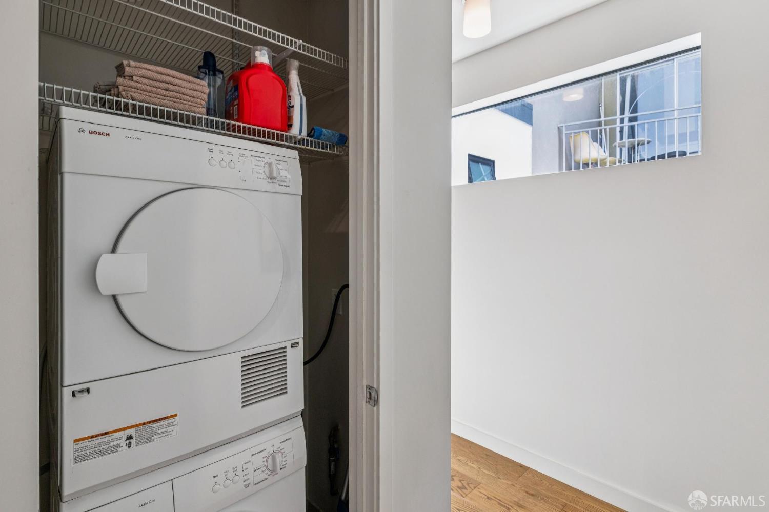 Laundry closet with stacked Bosch washer and dryer beneath wire shelves of towels and cleaning supplies.