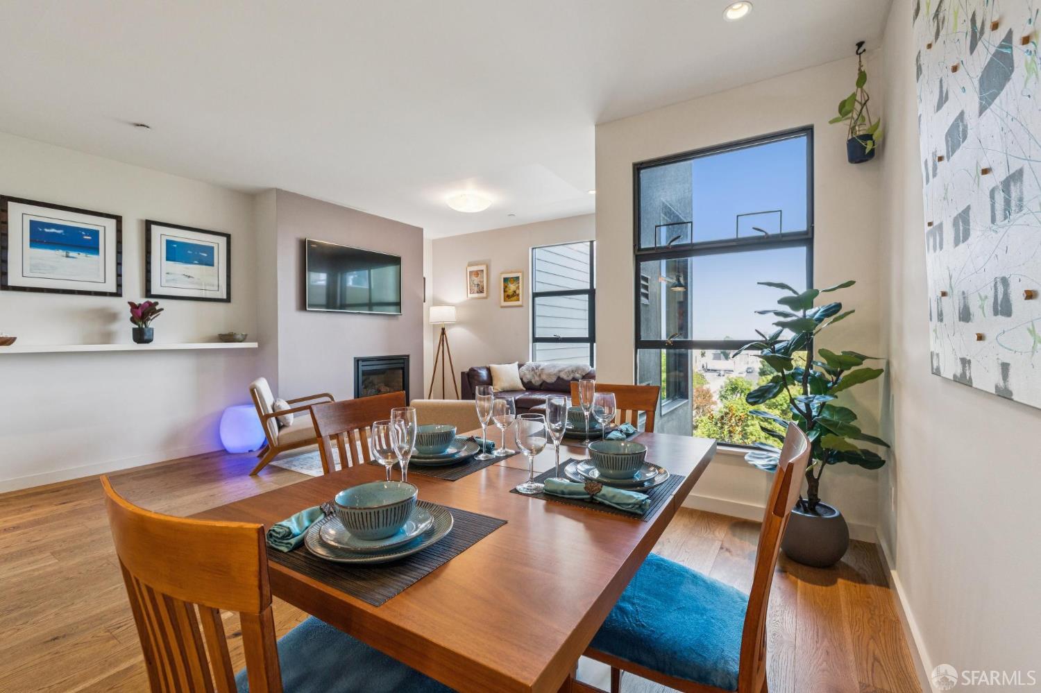 Dining area with a set wooden table, adjoining living room, fireplace, and tall windows.