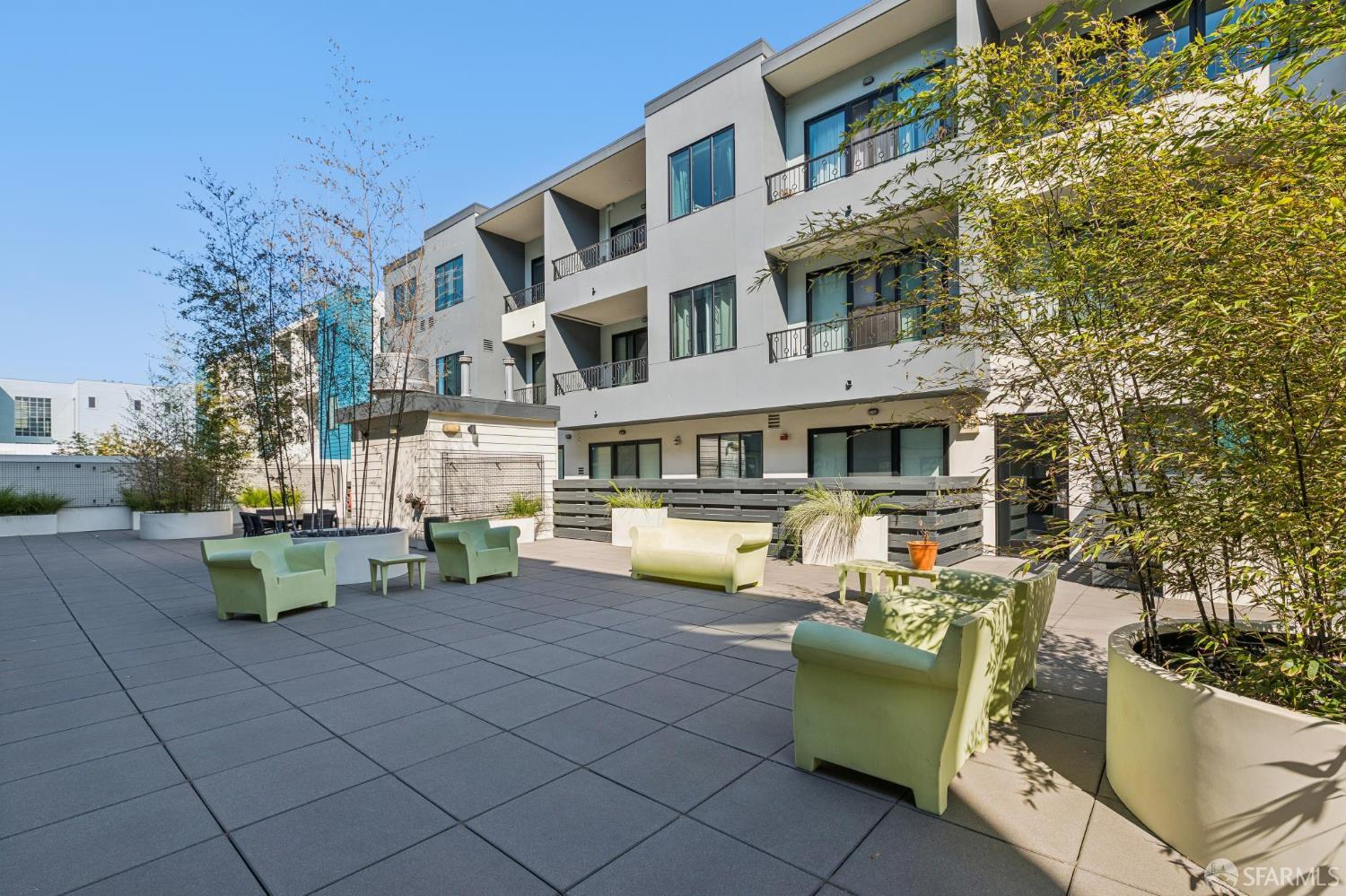 Condominium courtyard with pale green lounge chairs, large planters, and a paved patio.