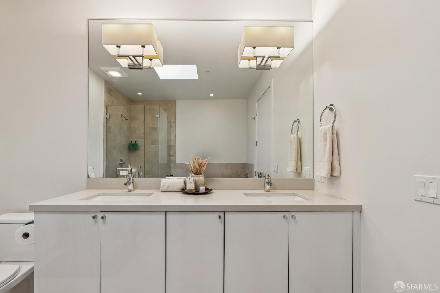 Modern bathroom with a white double vanity, large mirror, and glass-enclosed tiled shower.