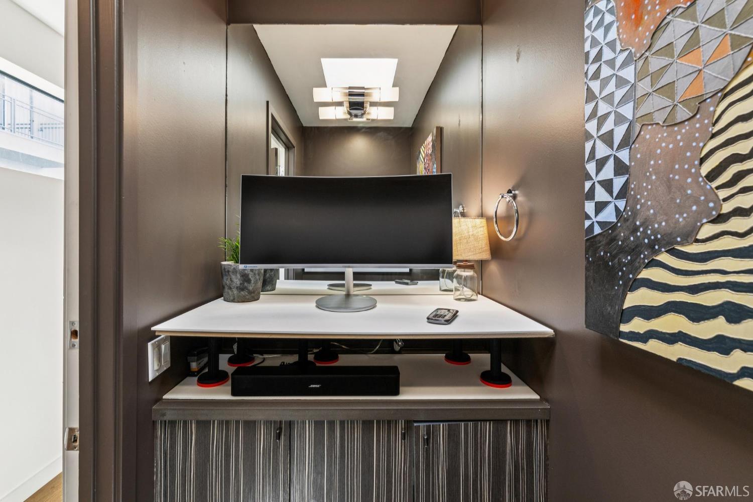 Built-in office nook with a large monitor, white desk, and patterned wall art.