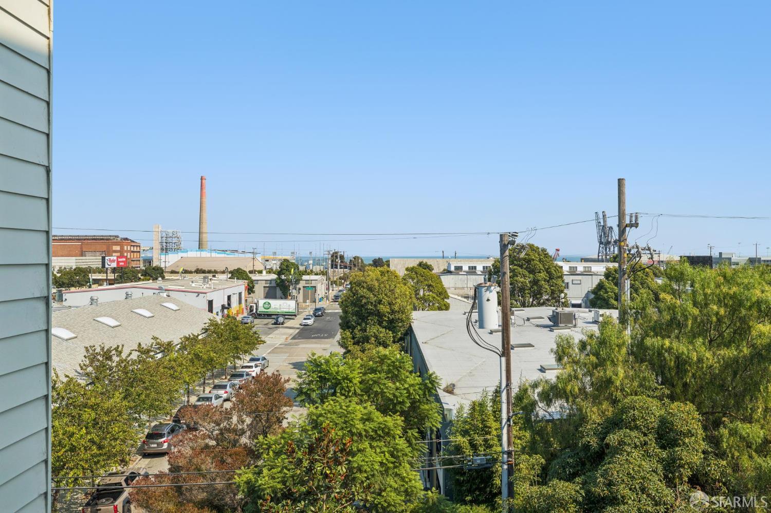 Elevated neighborhood view with industrial rooftops, a brick smokestack, and water on the horizon.