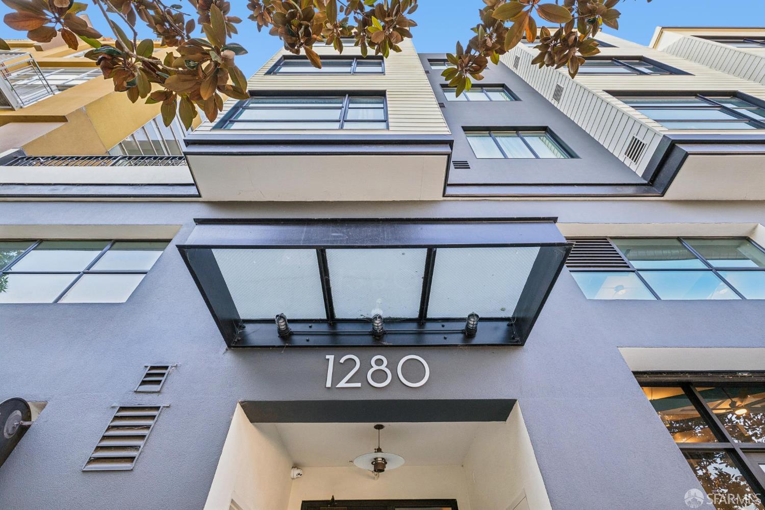 Modern residential building entrance with the number 1280 beneath upper-story windows and leafy branches.