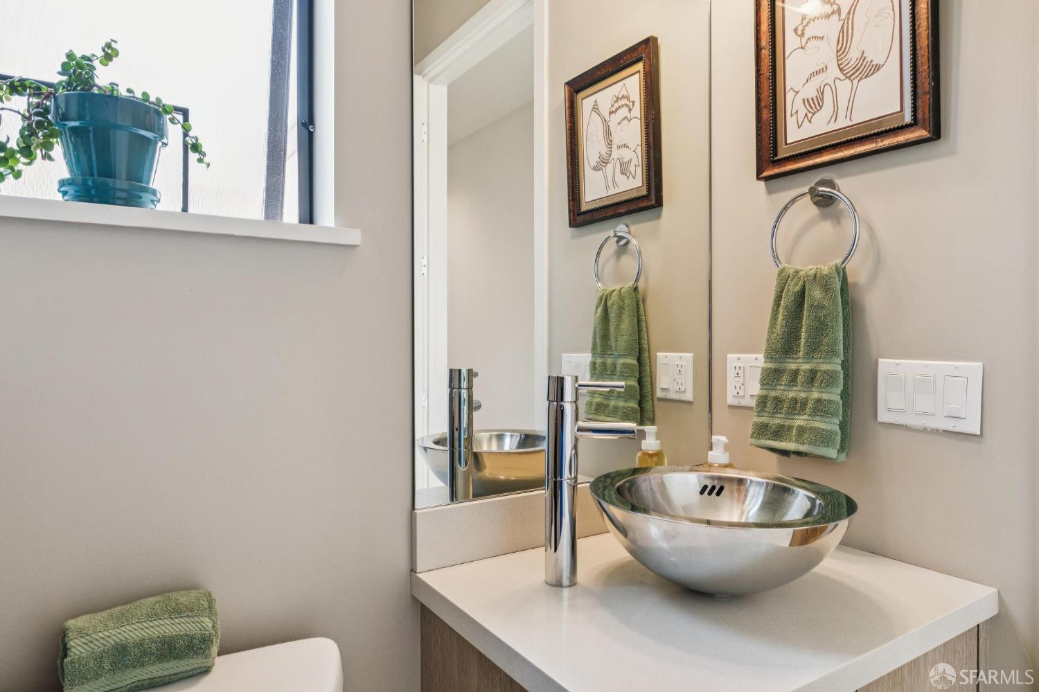 Bathroom vanity with a metal vessel sink, tall chrome faucet, and green towels beside a large mirror.